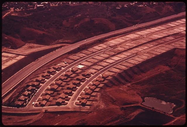 Aerial view of a suburban housing development with homes and empty graded lots alongside a highway.