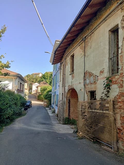 Narrow street in Migliandolo, Piedmont, Italy, with distressed old buildings and greenery.