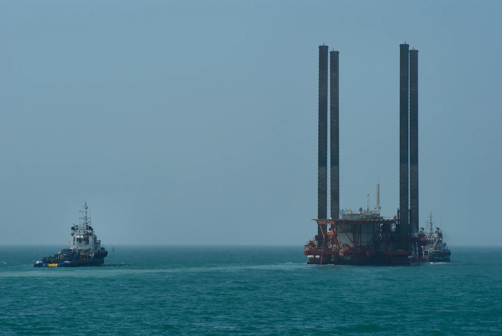 An oil rig is being towed across a body of water by a tugboat.