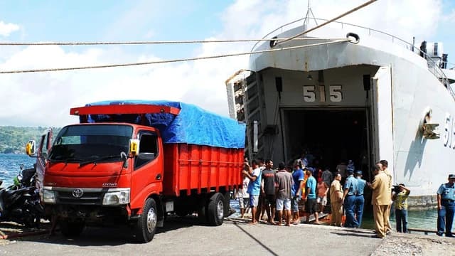 KRI Teluk Sampit-515 ship being loaded with rice by people and a red truck.