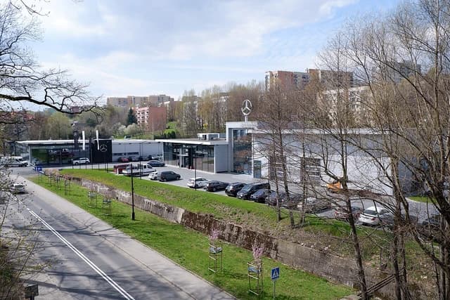 Mercedes-Benz dealership building with cars parked outside along a street.