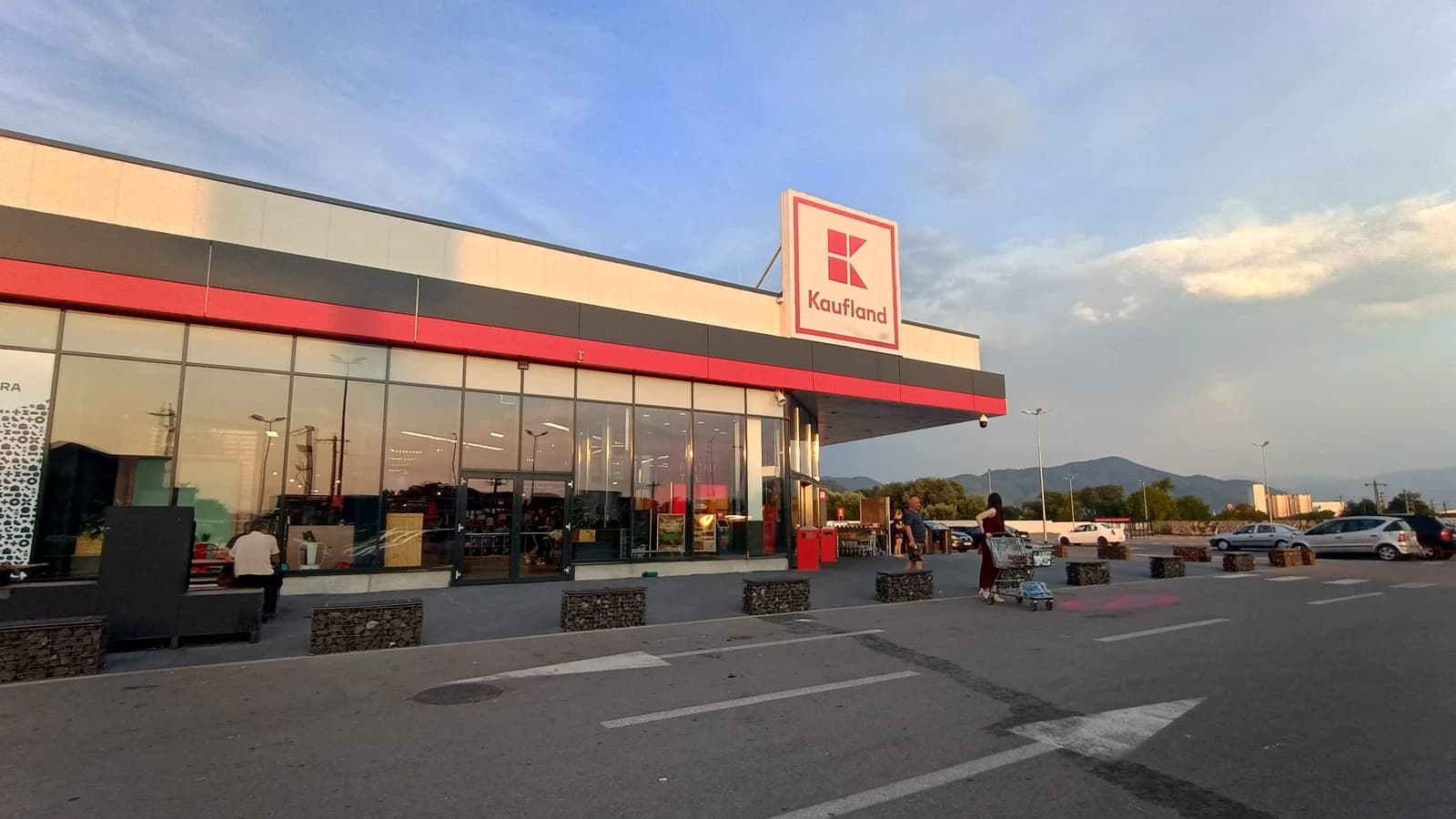 Kaufland supermarket exterior in Hateg, Romania, with parking area and distant mountains.