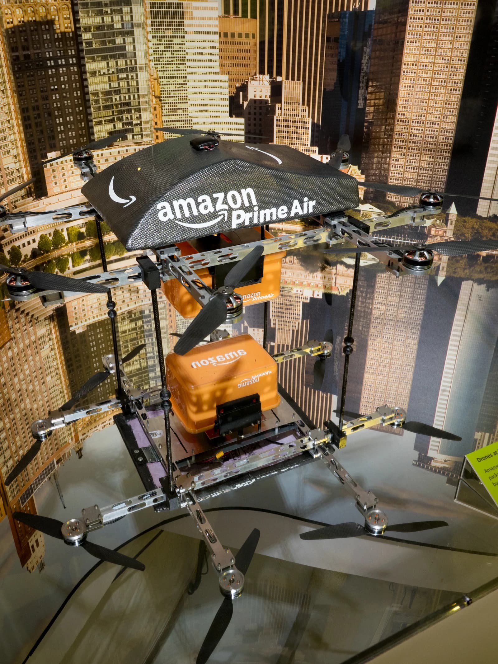 Amazon Prime Air delivery drone with package and cityscape backdrop.
