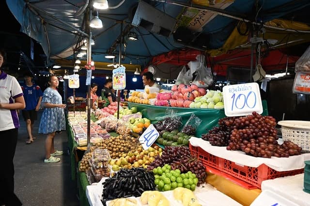 Shoppers browse a fruit stall at a busy night market, overflowing with fresh produce.