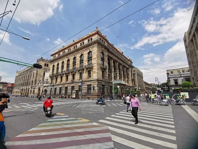 People crossing a street in front of the Bank of Mexico building.