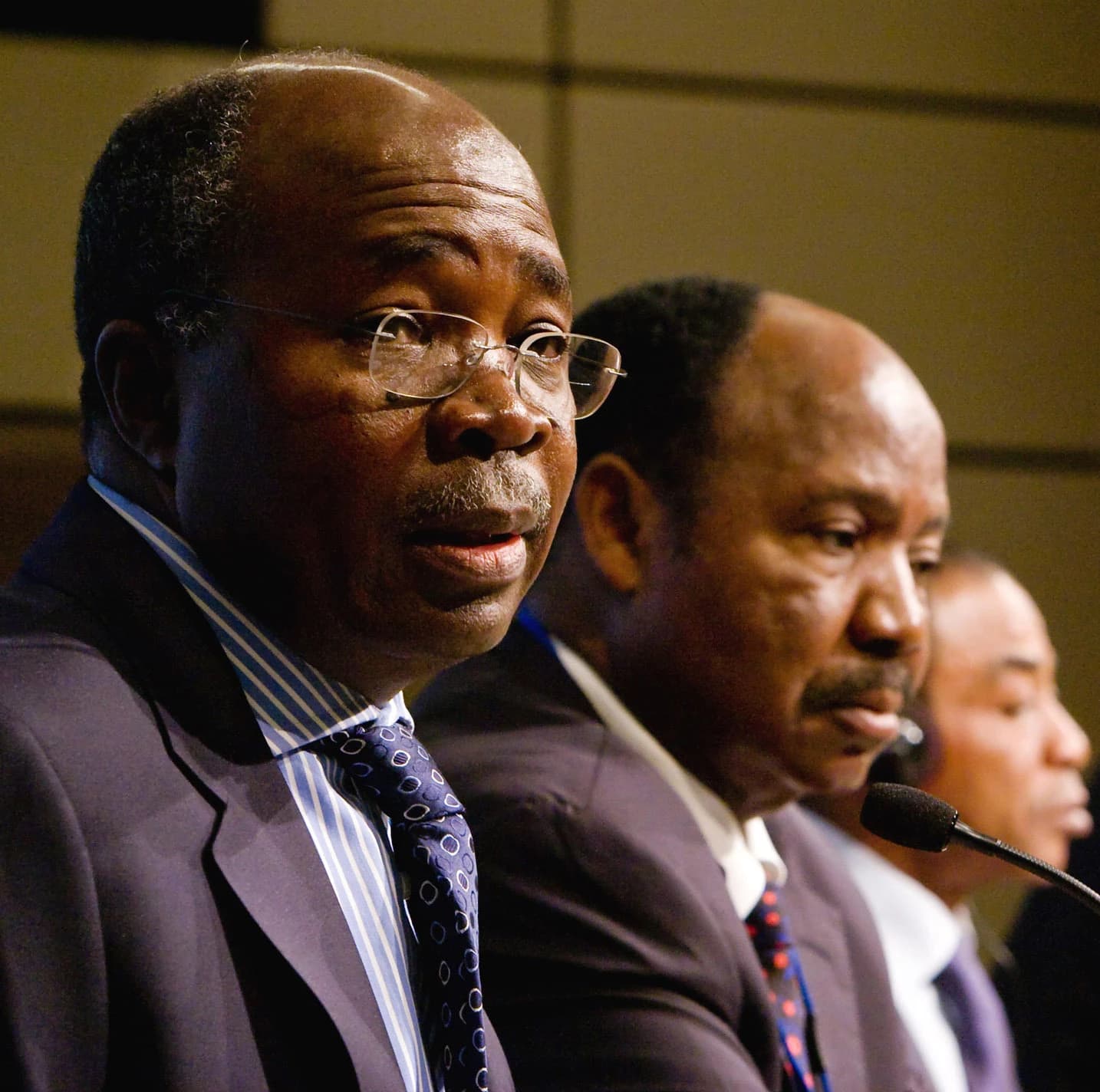 An African finance minister, wearing glasses, speaks at a conference podium.