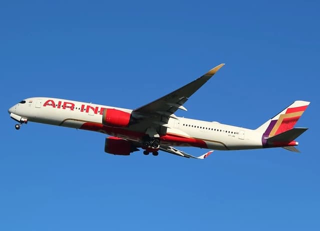 An Air India airplane, registration VT-JRE, flying in a clear blue sky.