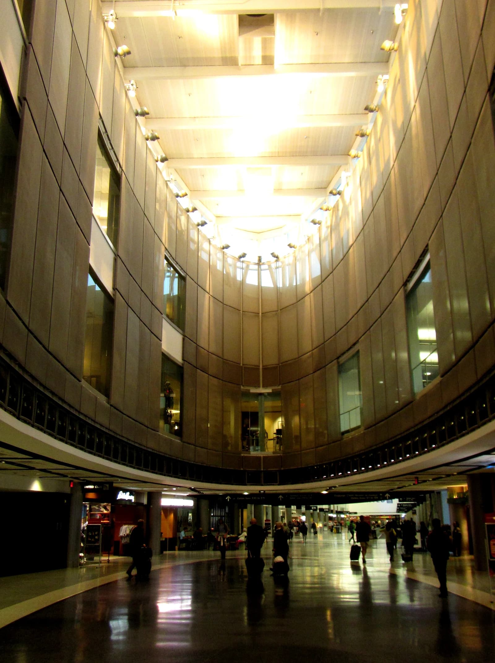 Travelers with luggage walk through the brightly lit George Bush Intercontinental Airport Terminal E.