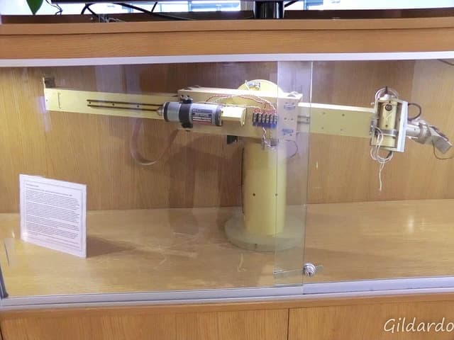 The Stanford Arm, an early robotic arm, displayed in a glass case with an informational plaque.
