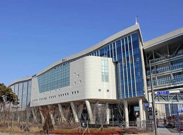 Modern building with glass and light-colored panels, under a clear blue sky.