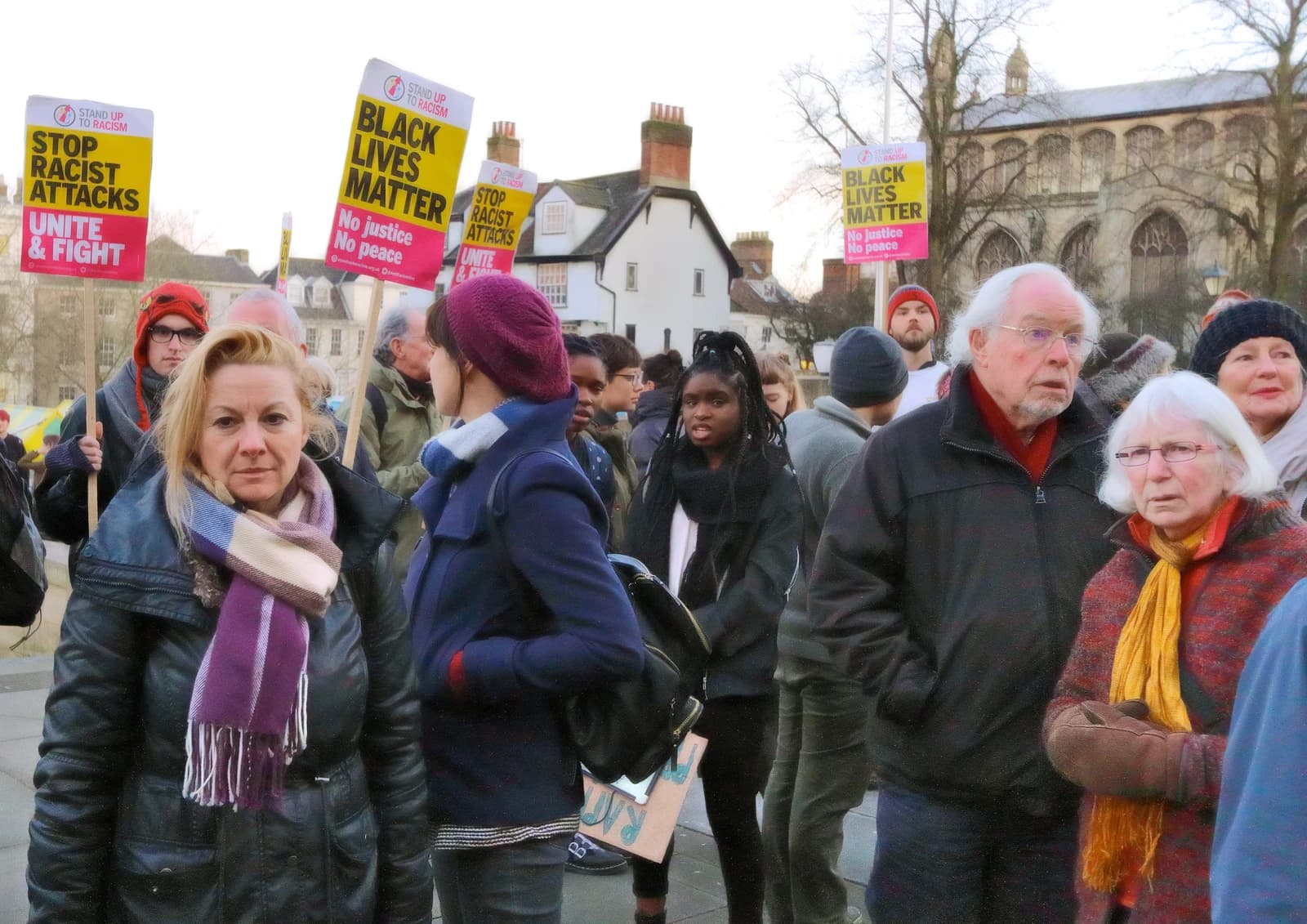 People holding signs that read "Black Lives Matter" and "Stop Racist Attacks" at a protest.