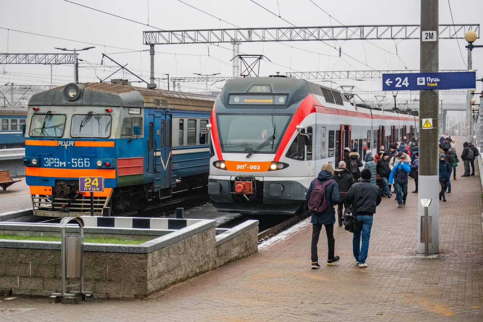 Two passenger trains, an older blue model and a newer red and white model, at a railway station.
