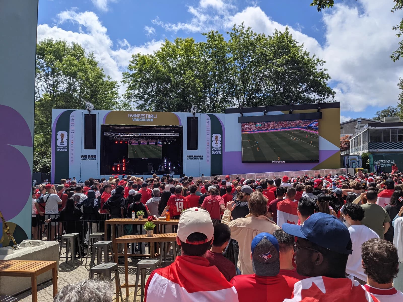 People gathered outdoors watching a soccer match on a large screen at a fan festival.