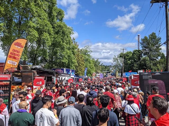 Large crowd of people gathered outdoors at Hastings Park, Vancouver, with food stalls.