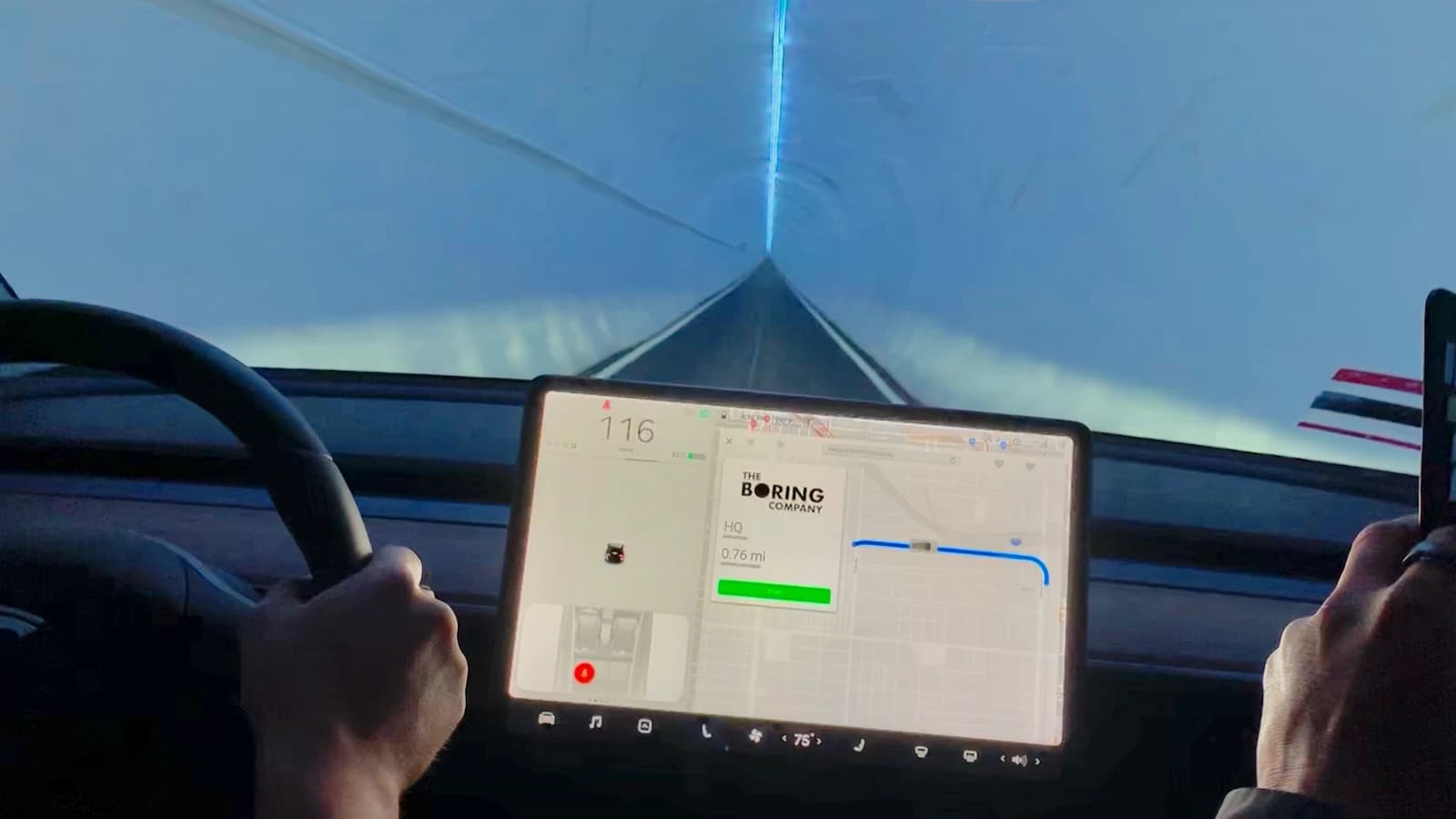 Person's hands on a Tesla steering wheel in a tunnel, showing the car's display.