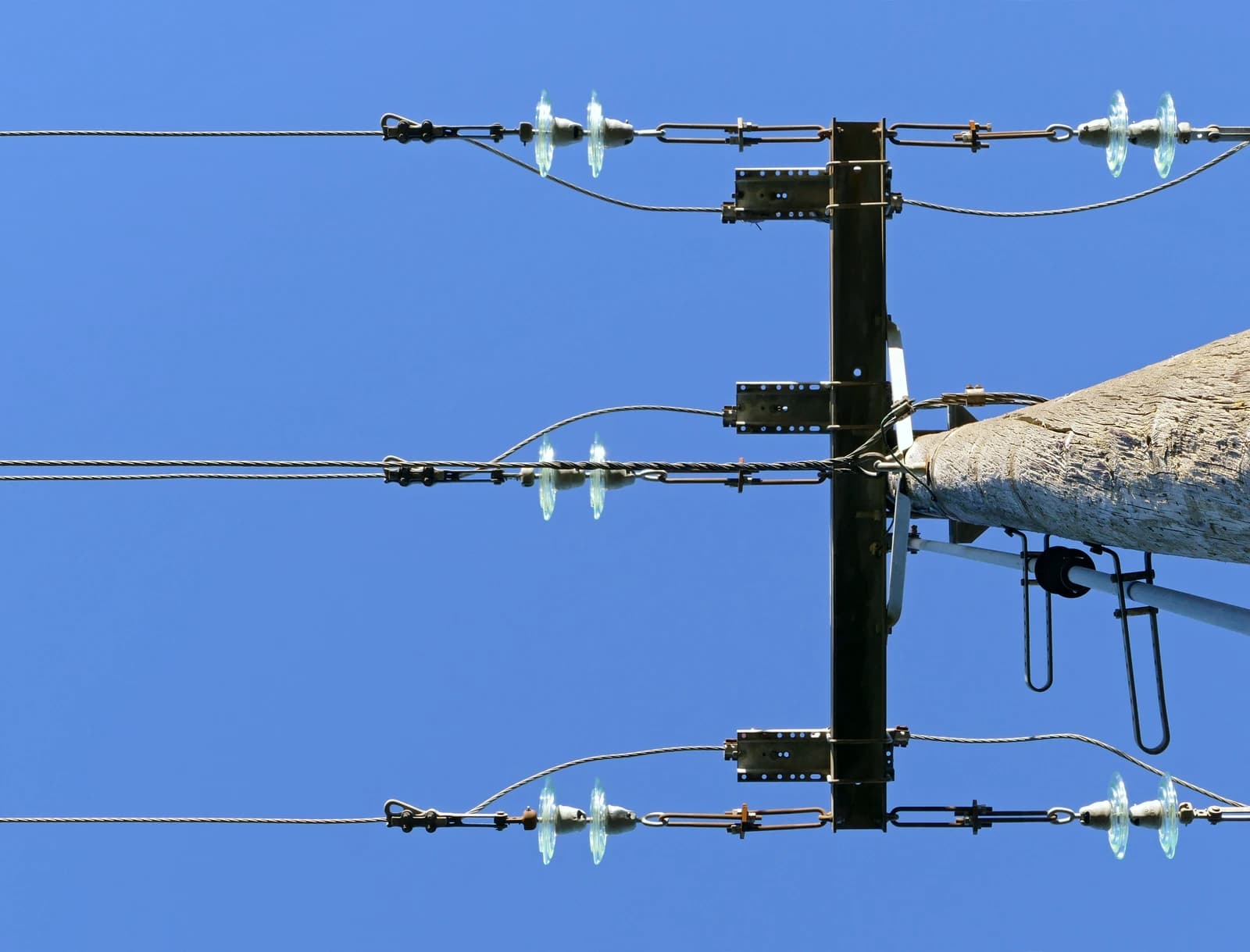 Power lines and insulators attached to the top of a utility pole against a blue sky.
