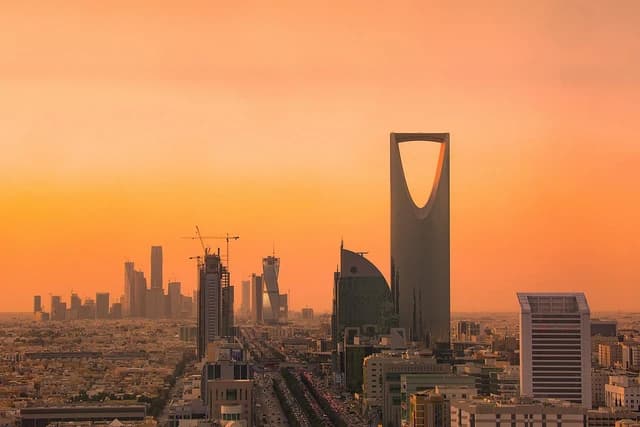 Riyadh's skyline at sunset featuring the Kingdom Centre skyscraper and other buildings.