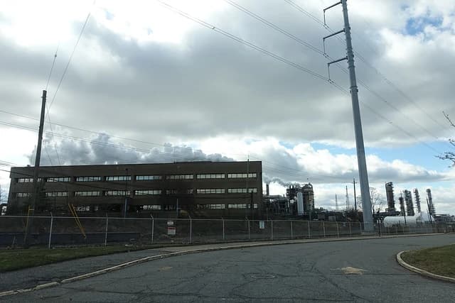 Bayway Refinery, a large industrial complex with buildings and smokestacks under a cloudy sky.