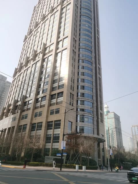 Modern high-rise building with a curved glass facade and beige exterior walls.