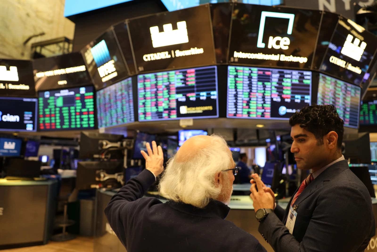 Two financial traders discuss market conditions on a trading floor.