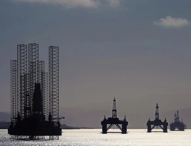 Several silhouetted oil rigs and platforms partially submerged in water, under a cloudy sky.