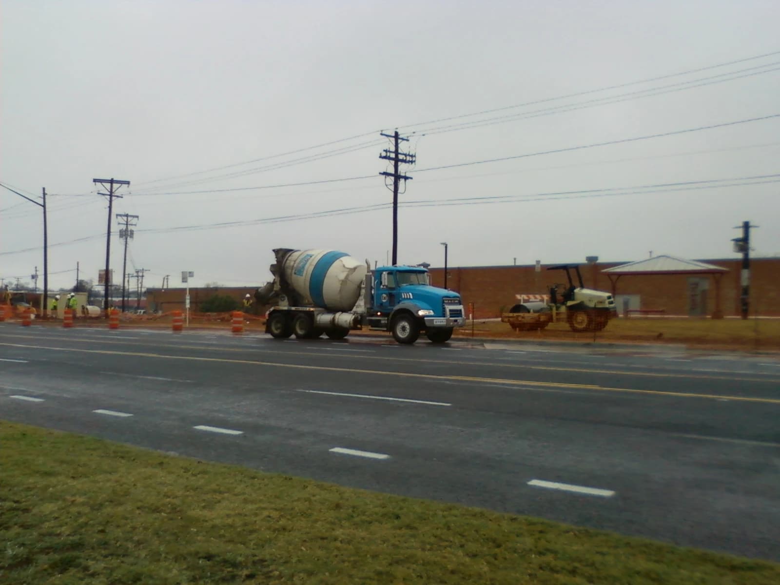 A cement mixer truck parked next to a construction site with orange cones and utility poles.