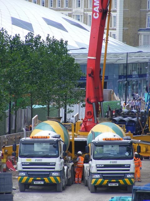 Two white and green Lafarge DAF cement mixer trucks parked at a construction site.