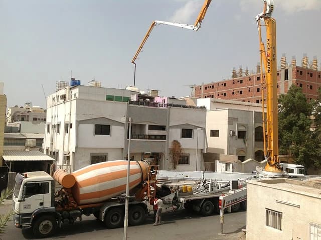Concrete mixer truck delivering cement to a construction site with a boom pump extended.