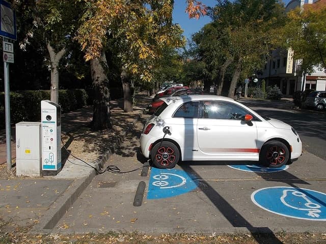 White Fiat 500e electric car plugged into a public charging station.