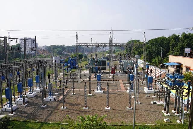 Electrical substation with transformers, insulators, and overhead power lines in a rural setting.