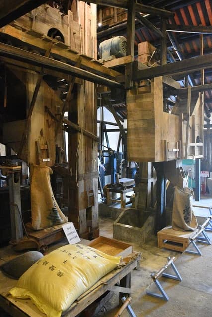 Interior of an old-fashioned rice mill showing wooden machinery and sacks of rice.