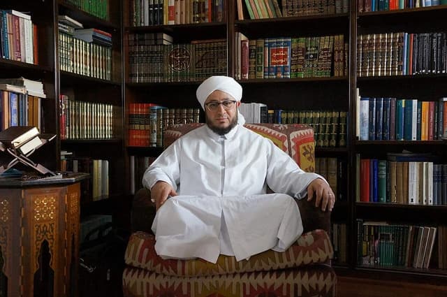 Azhari sitting in a patterned armchair in a library or office.