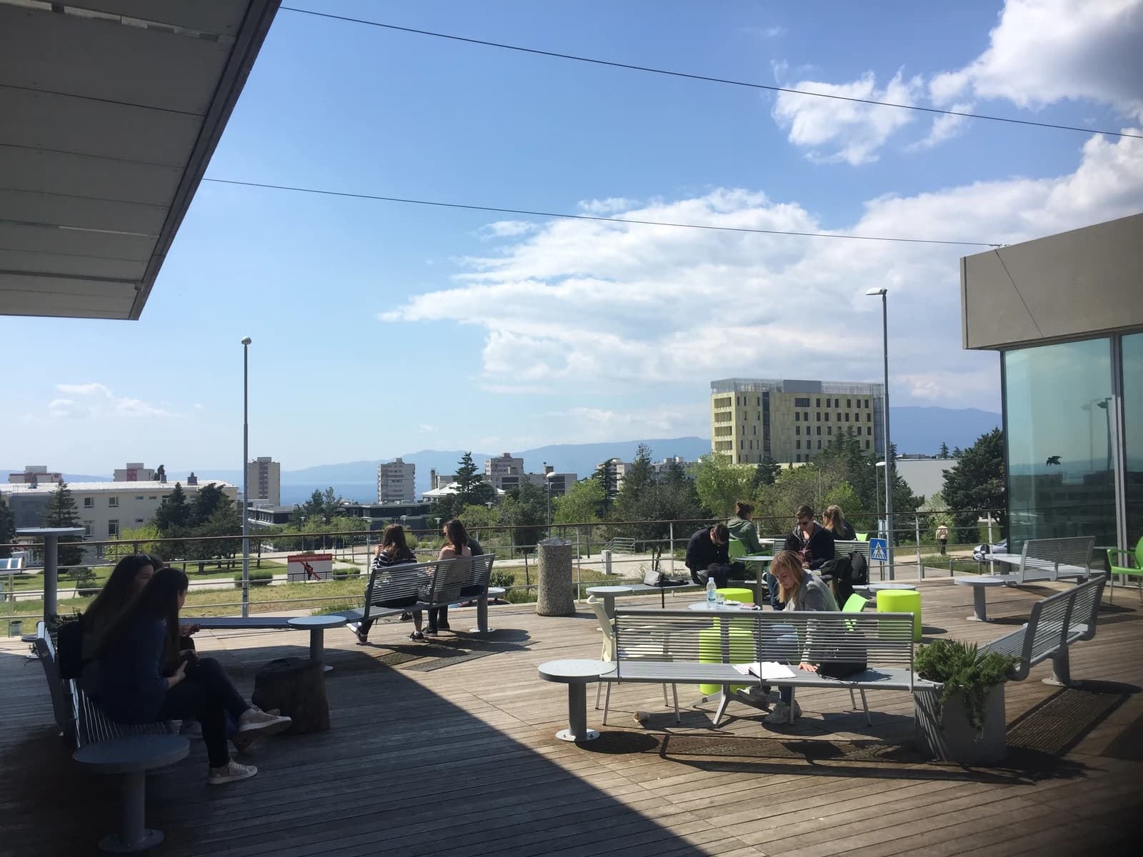 Students sitting at outdoor tables and benches on a university campus.