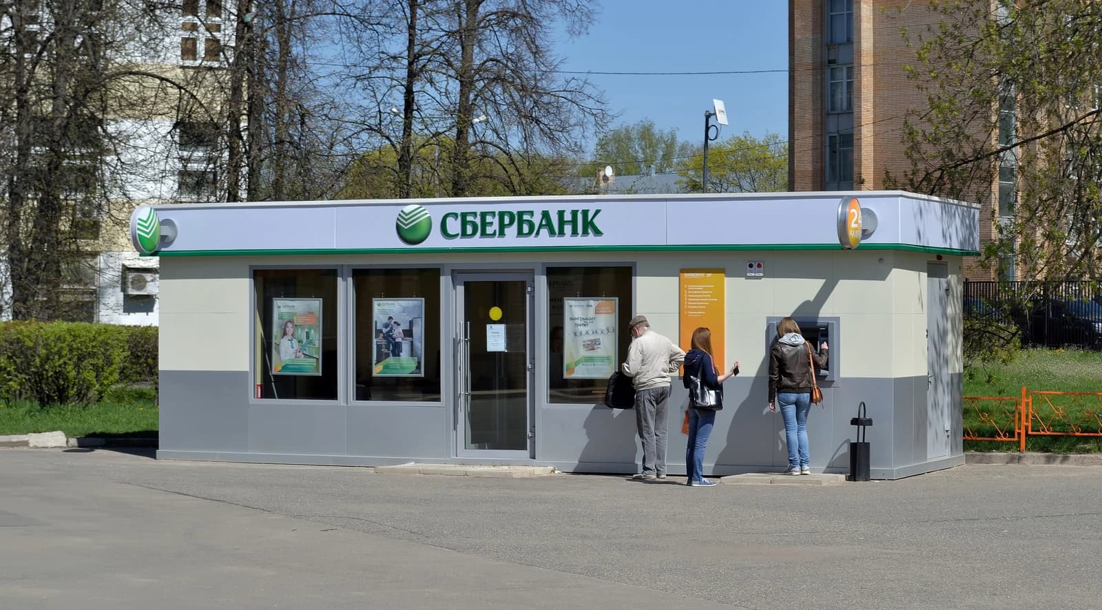 People using an ATM and standing near the entrance of a Sberbank branch.