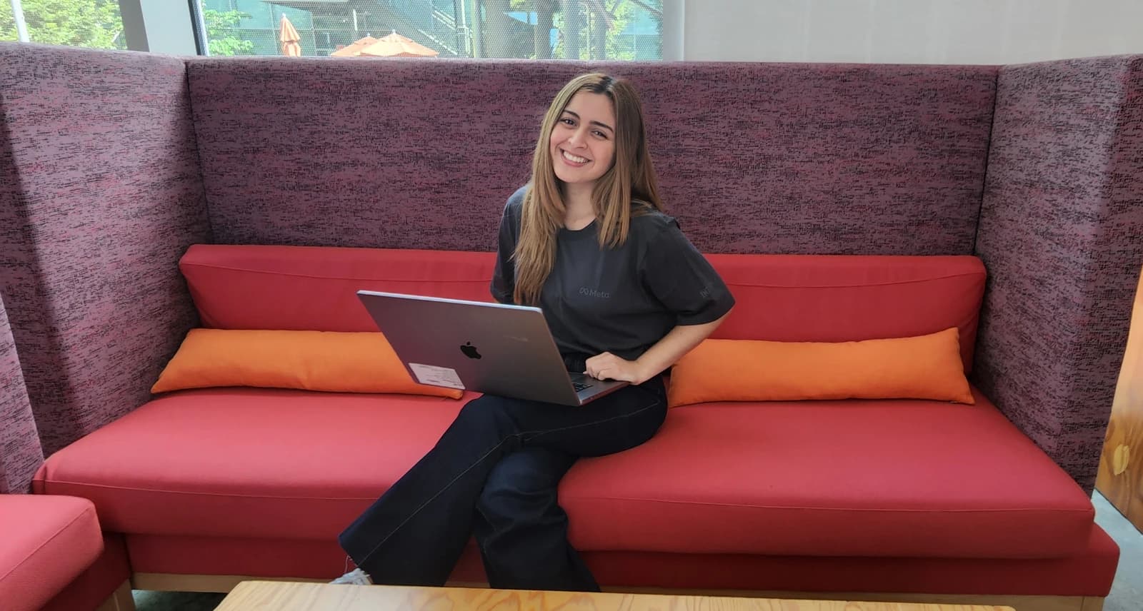 Diana Vicezar, Meta Product Design, sitting on a red sofa with an open laptop.