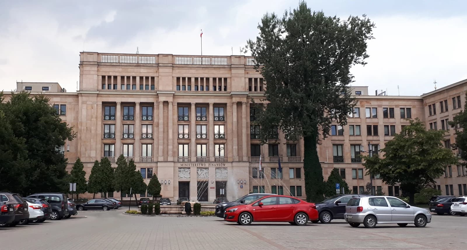 Polish Ministry of Finance building exterior with parked cars and trees.