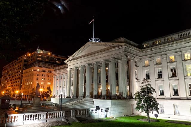 U.S. Treasury Department building exterior at night with illuminated windows.
