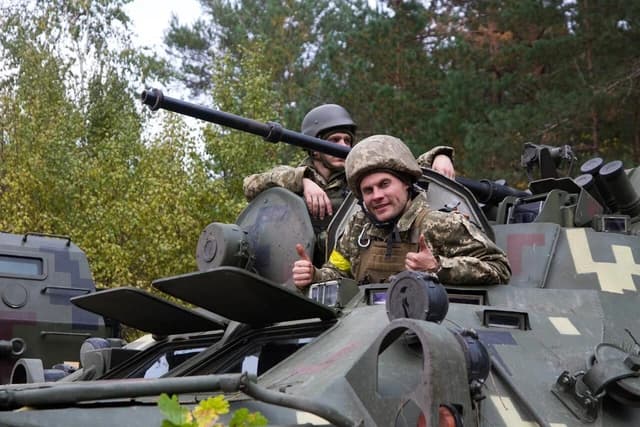 Ukrainian soldiers wearing camouflage uniforms and helmets in a military vehicle.