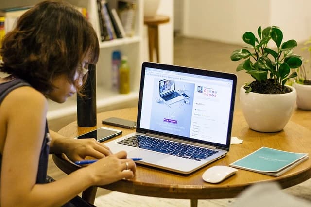 Person taking notes at a coffee table with a laptop and phone.