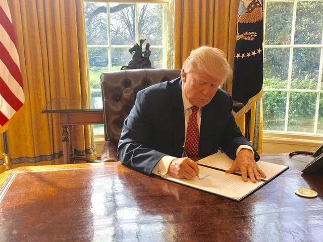 Donald Trump, then US President, signing a document at a large wooden desk.