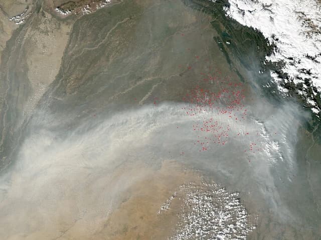 Satellite image showing widespread agricultural fires with red dots indicating fire locations and large smoke plumes over land.