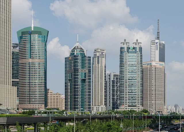 Modern skyscrapers rise against a blue sky with clouds in Lujiazui, Shanghai.