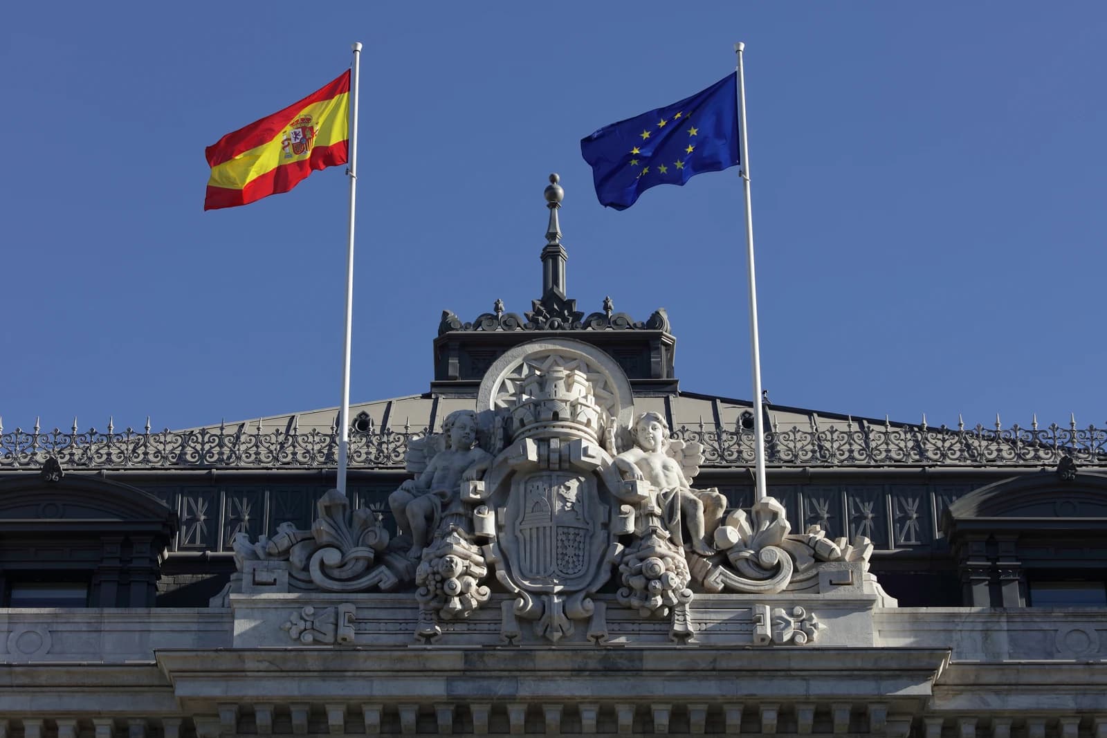 Spanish and European Union flags flying above the Banco de España building in Madrid.
