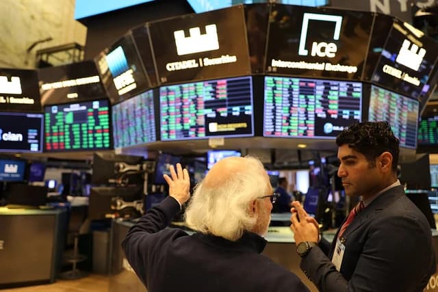 Two men, one with white hair, one with dark hair, talking on a trading floor.