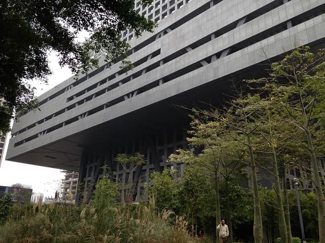 The modern, geometric building of the Shenzhen Stock Exchange partially obscured by trees.
