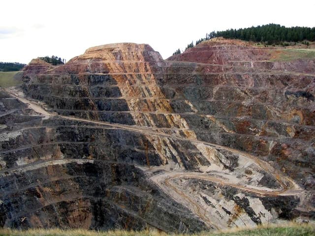 Homestake Mine Pit, a large terraced open-pit mine, with trees on the distant ridgeline.