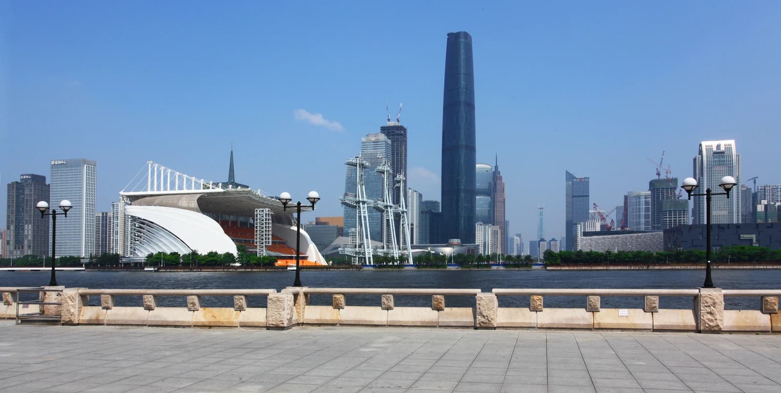 Modern skyline of Guangzhou, China, with a river and pedestrian area in the foreground.