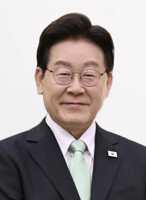 President Lee Jae-myung smiling and wearing a light green tie and eyeglasses.