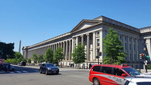Exterior of the U.S. Treasury Department building in Washington D.C., with street traffic.