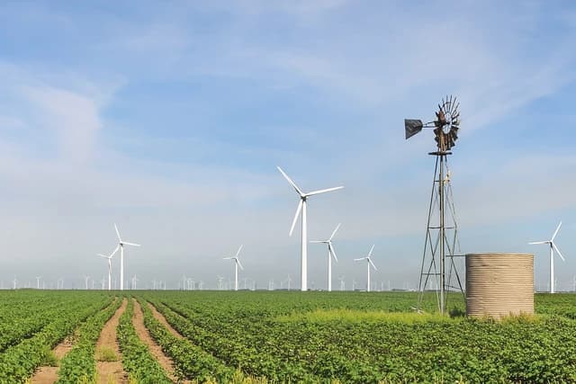 Wind turbines and an old-fashioned windmill stand in a green agricultural field under a blue sky.